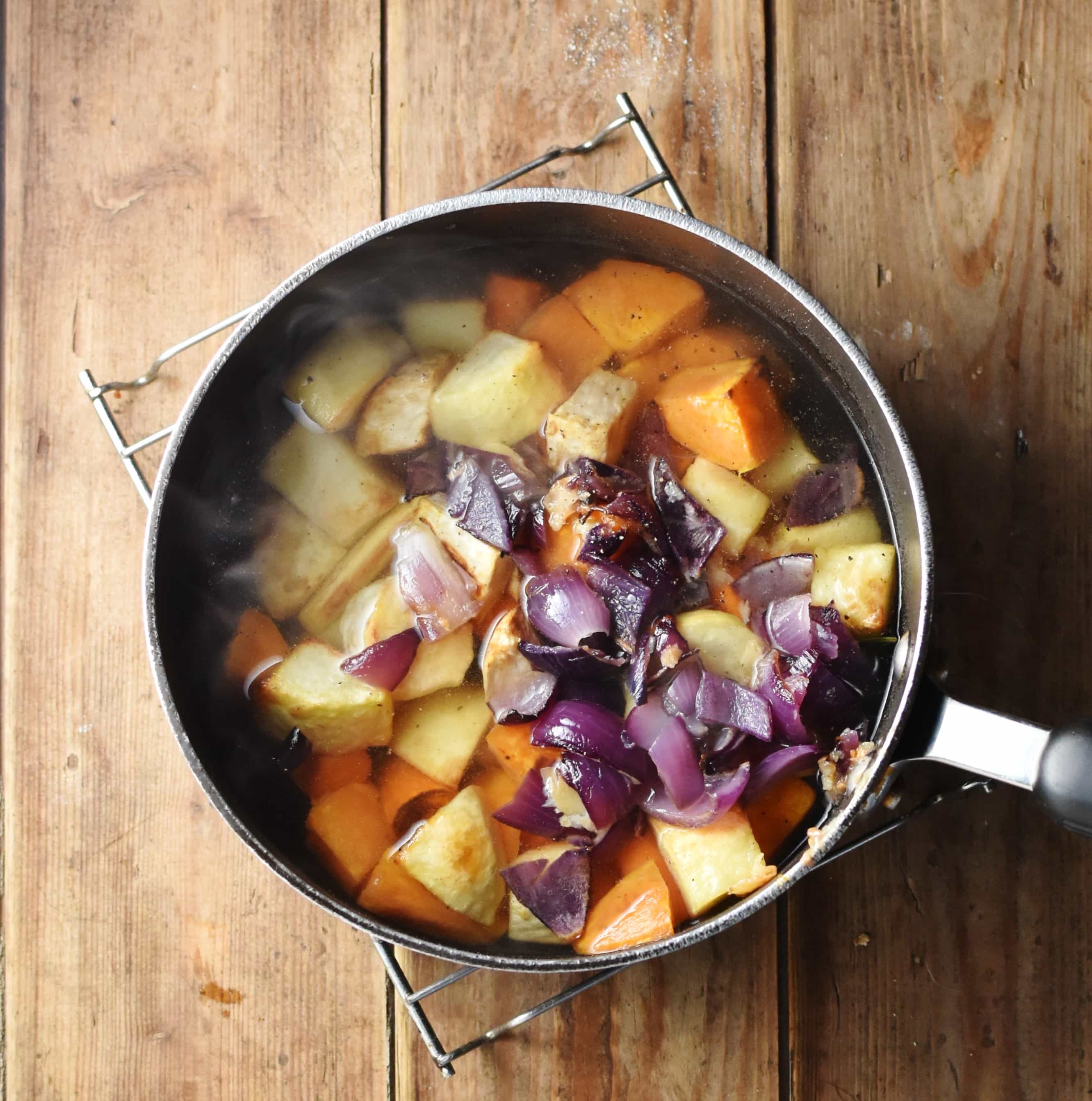Chunks of root vegetables and chopped red onion in large pot with water.