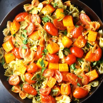 Top down view of pasta with chunks of butternut squash and tomato in pan.