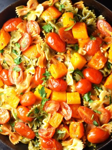 Top down view of pasta with chunks of butternut squash and tomato in pan.