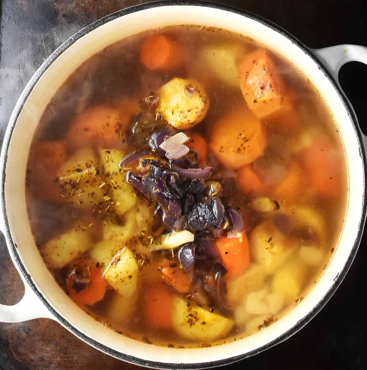 Top down view of vegetables in stock in large white pot.