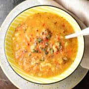Top down view of chunky root vegetable soup in yellow bowl with spoon on top of plate.