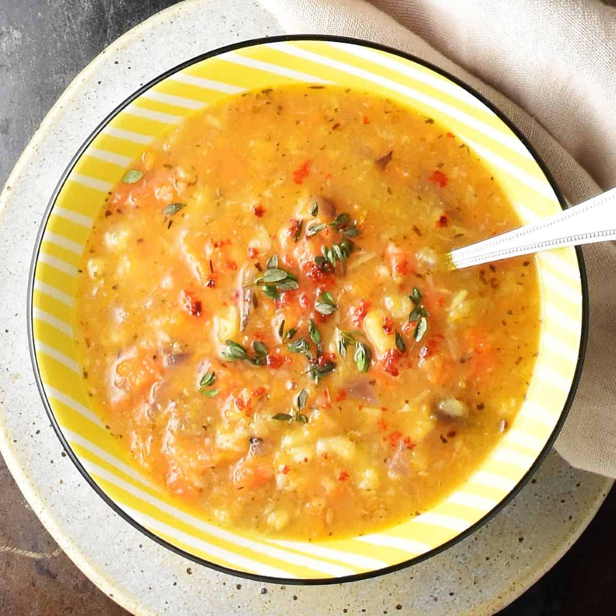 Top down view of chunky root vegetable soup in yellow bowl with spoon on top of plate.