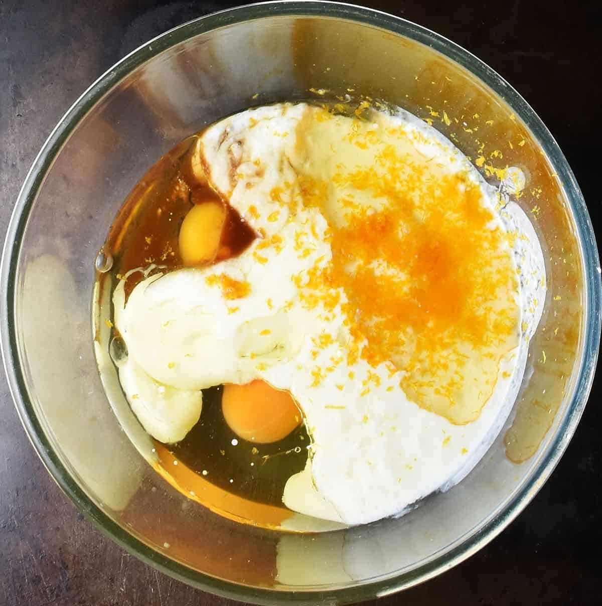 2 eggs, yogurt and orange zest in glass mixing bowl.