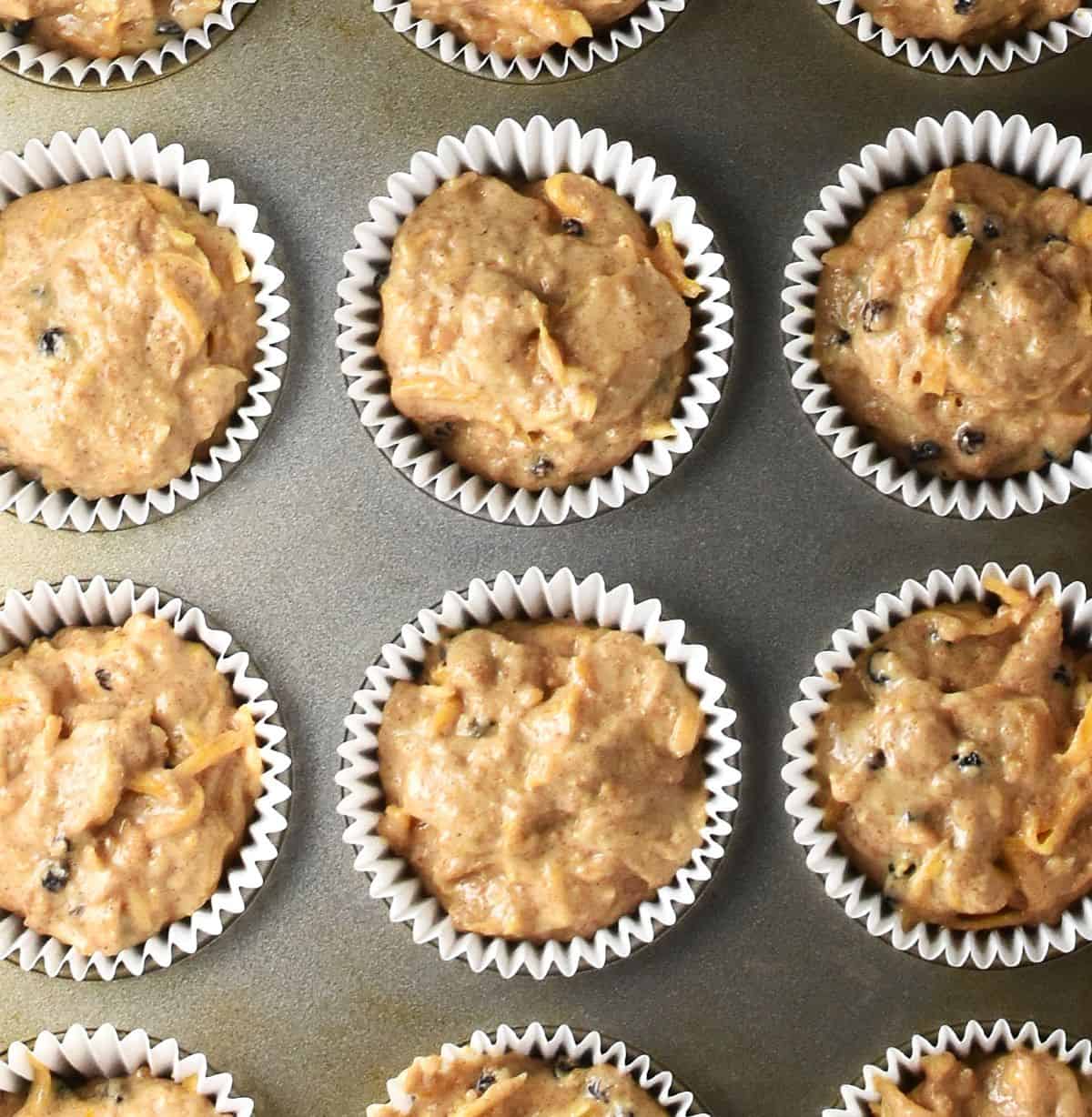 Top down view of raw squash muffin batter in white paper cases in muffin pan.