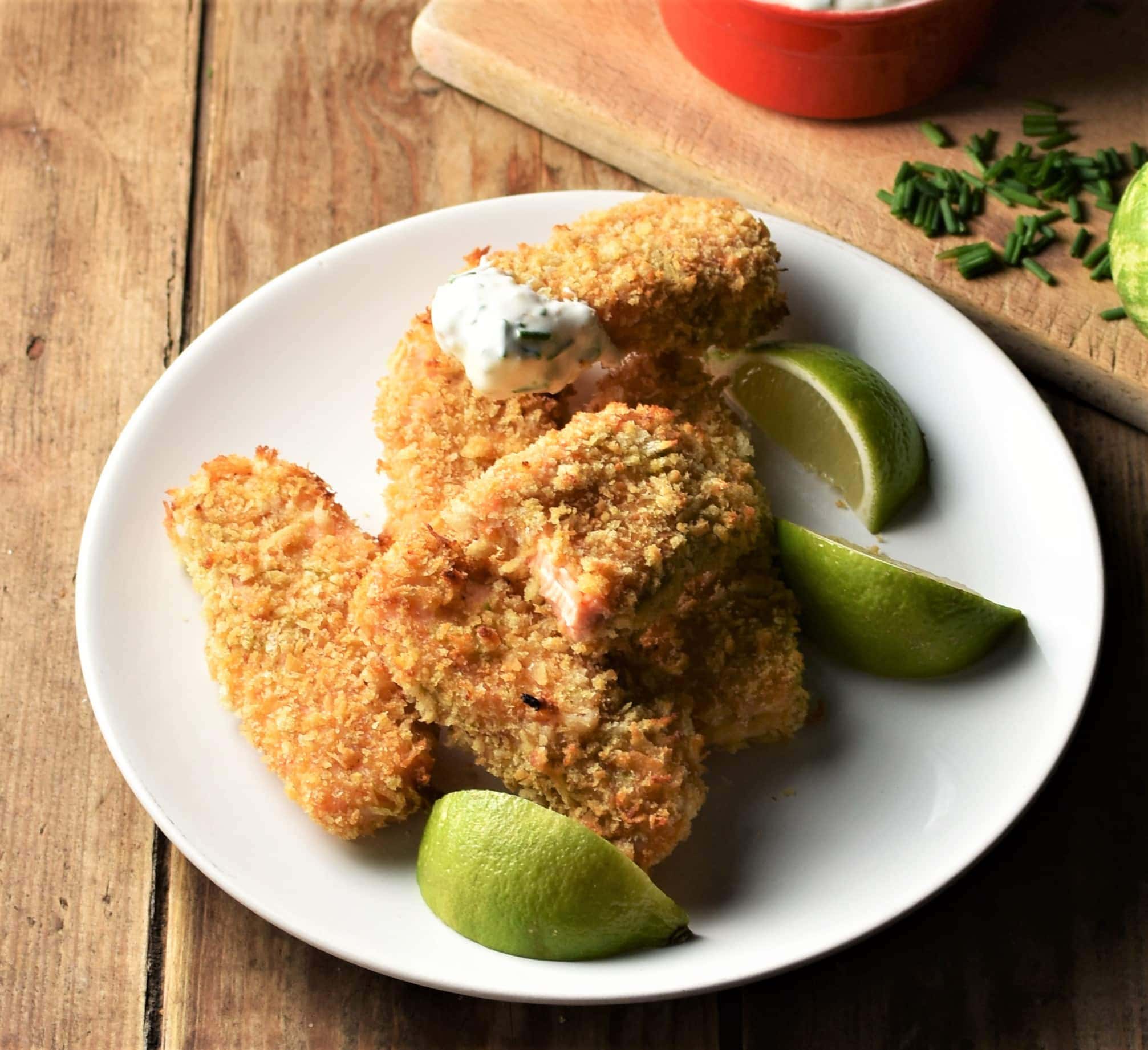 Breaded fish fingers on top of plate with lime wedges.