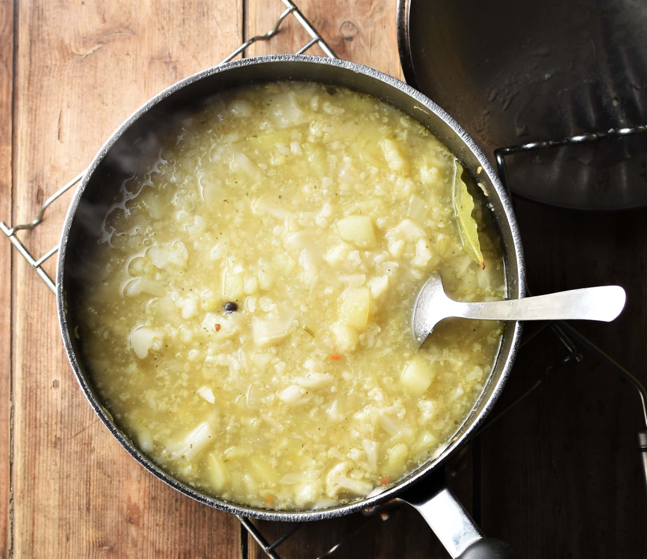 Chunky creamy cauliflower soup in large pot with spoon and potato masher to the right.