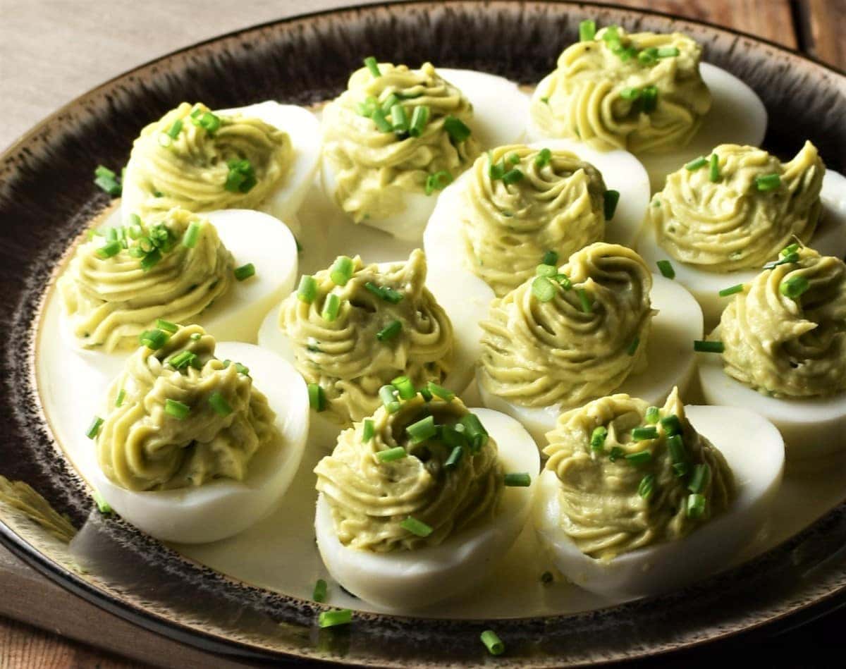 Close-up view of avocado deviled eggs on top of brown rimmed plate.