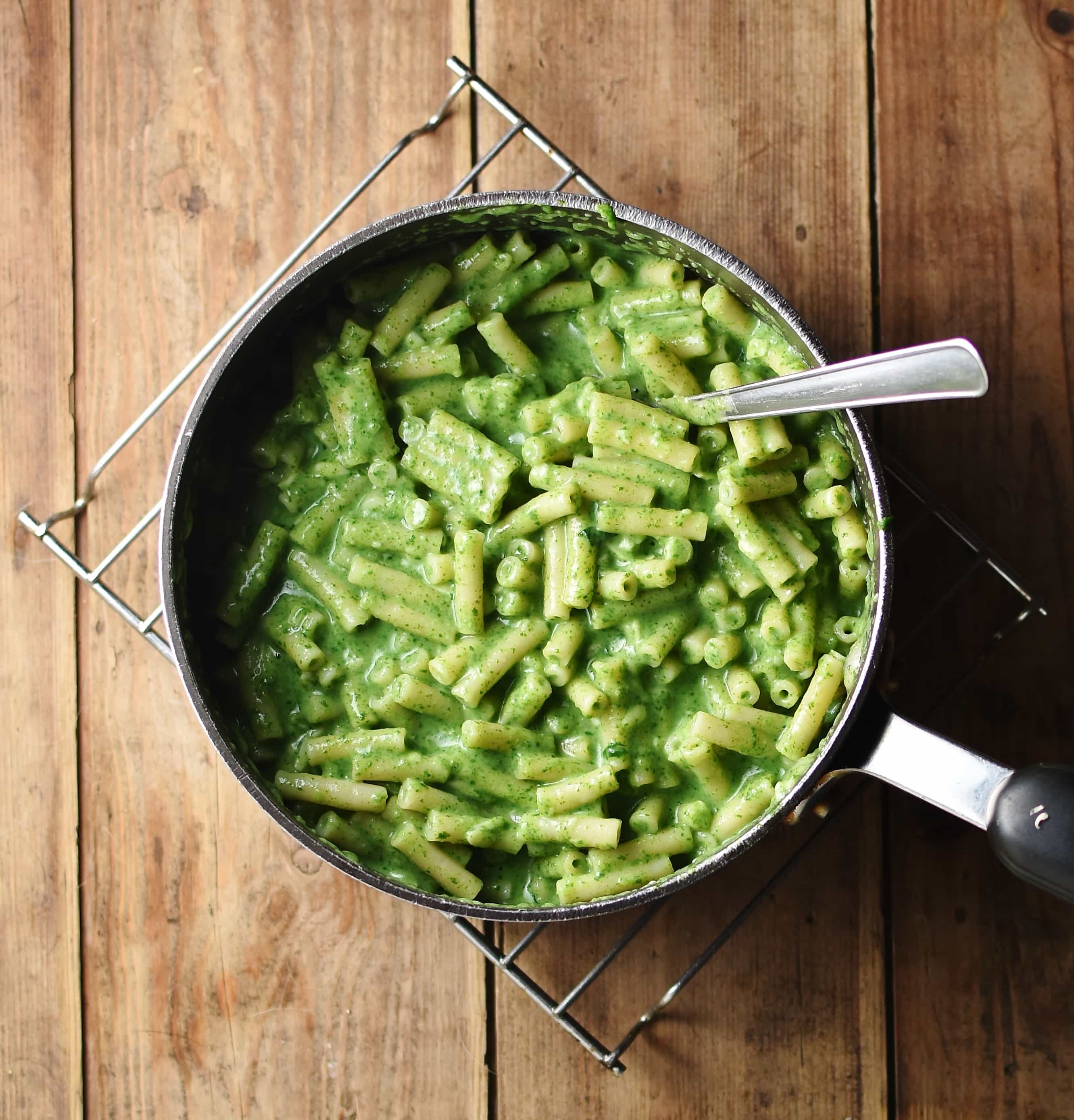 Spinach macaroni inside large pot with spoon on top of cooling rack.