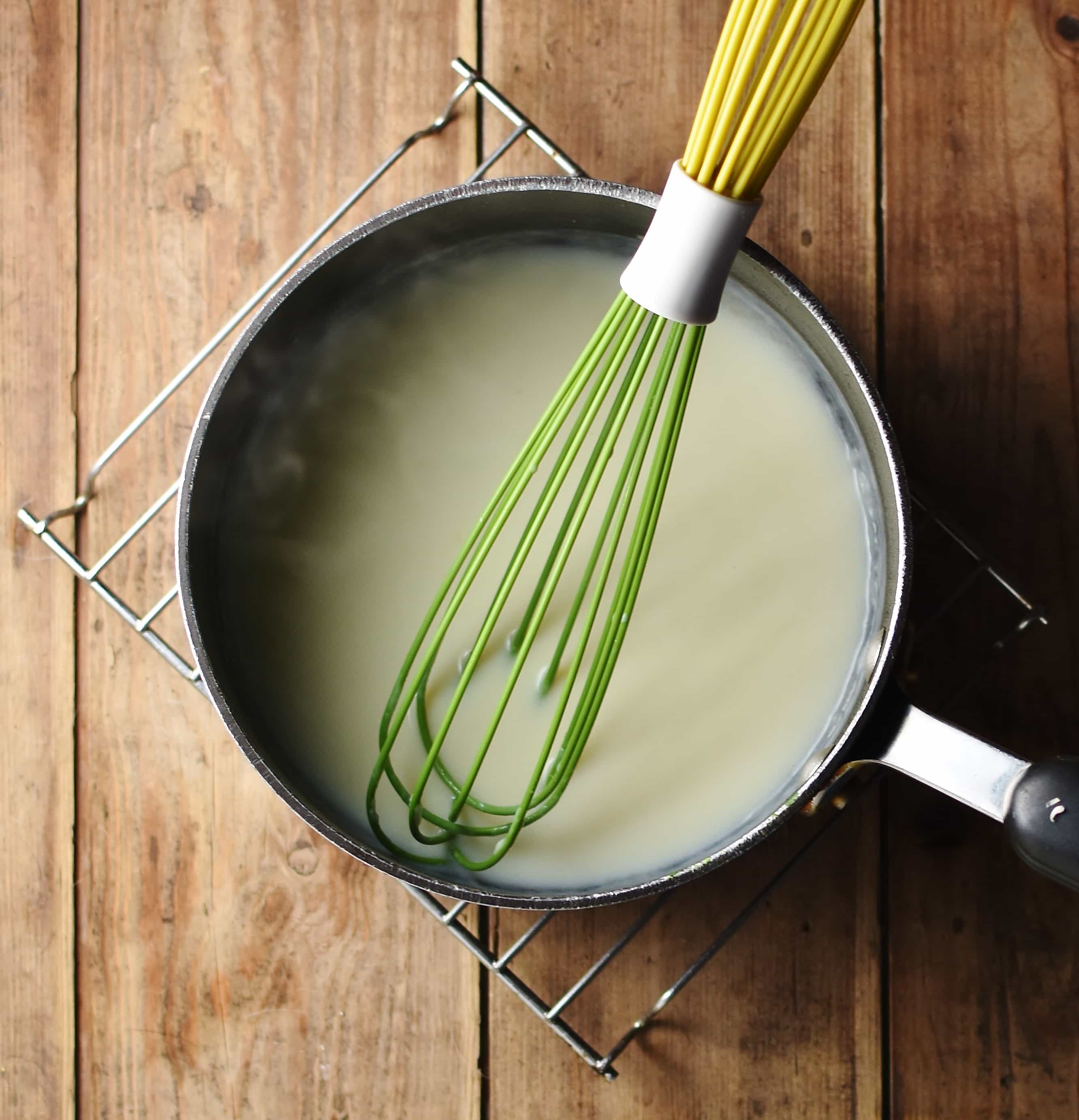 White sauce in large pot with green whisk on top of cooling rack.