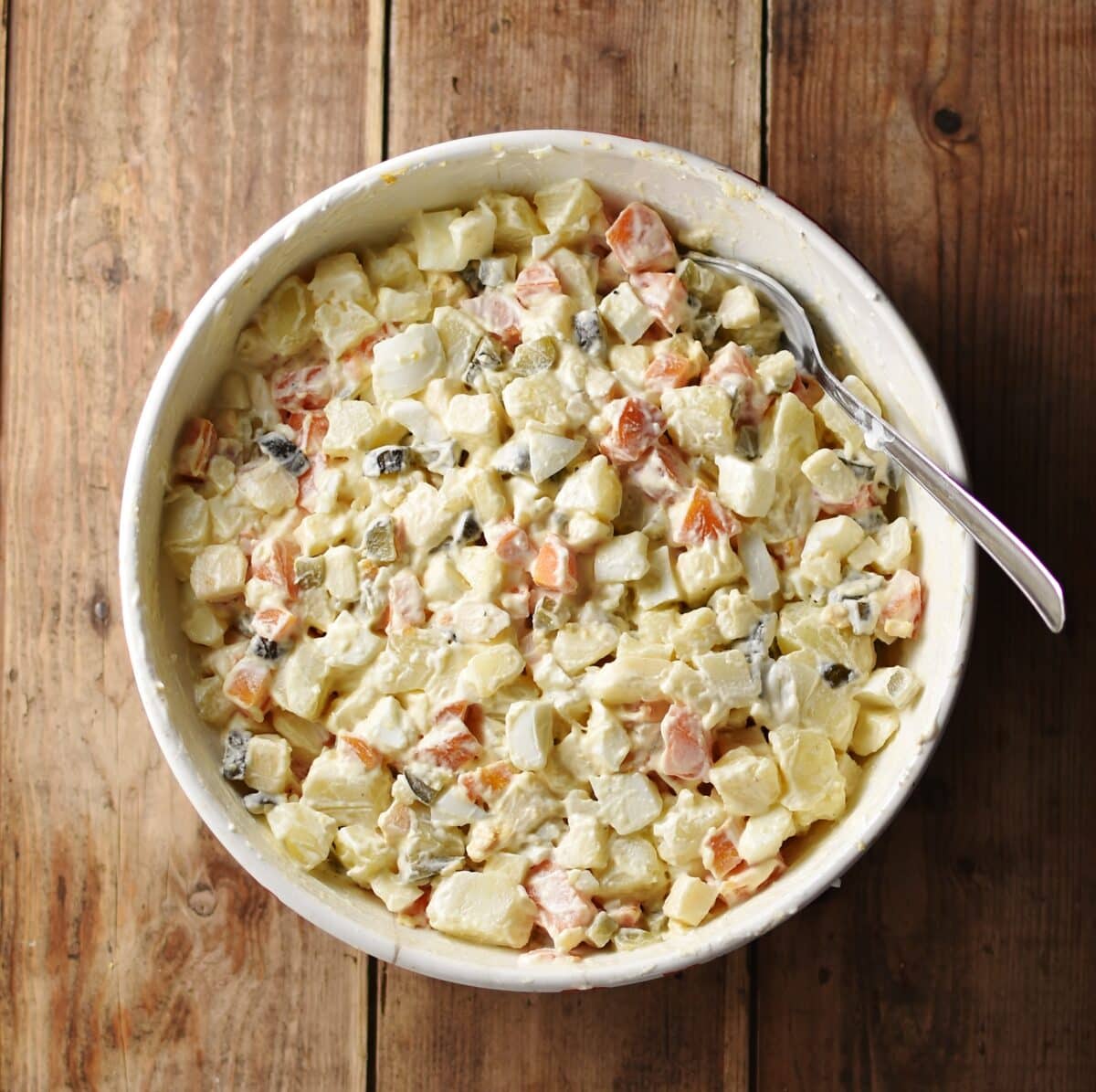 Top down view of potato salad with spoon inside large white bowl.