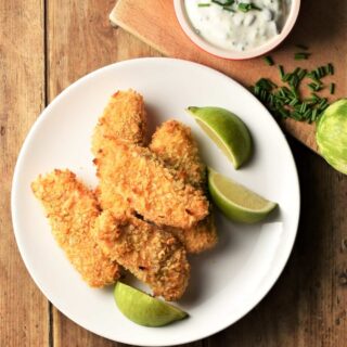 Breaded salmon fish fingers on top of plate with lime wedges.