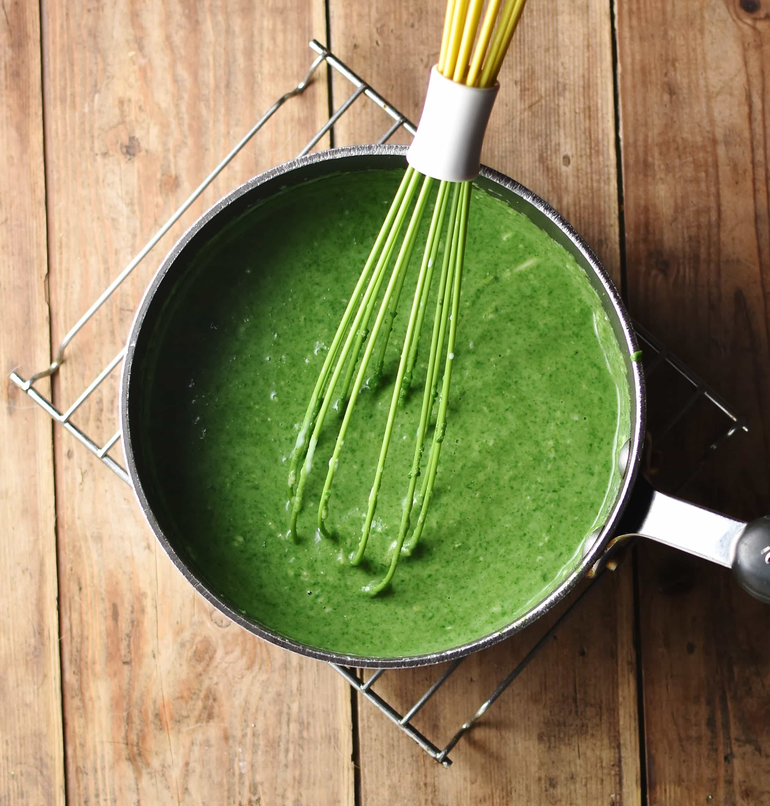 Top down view of spinach sauce inside large pot with green whisk.