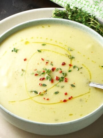 Side view of creamy cauliflower leek and potato soup in green bowl with fresh thyme in background.