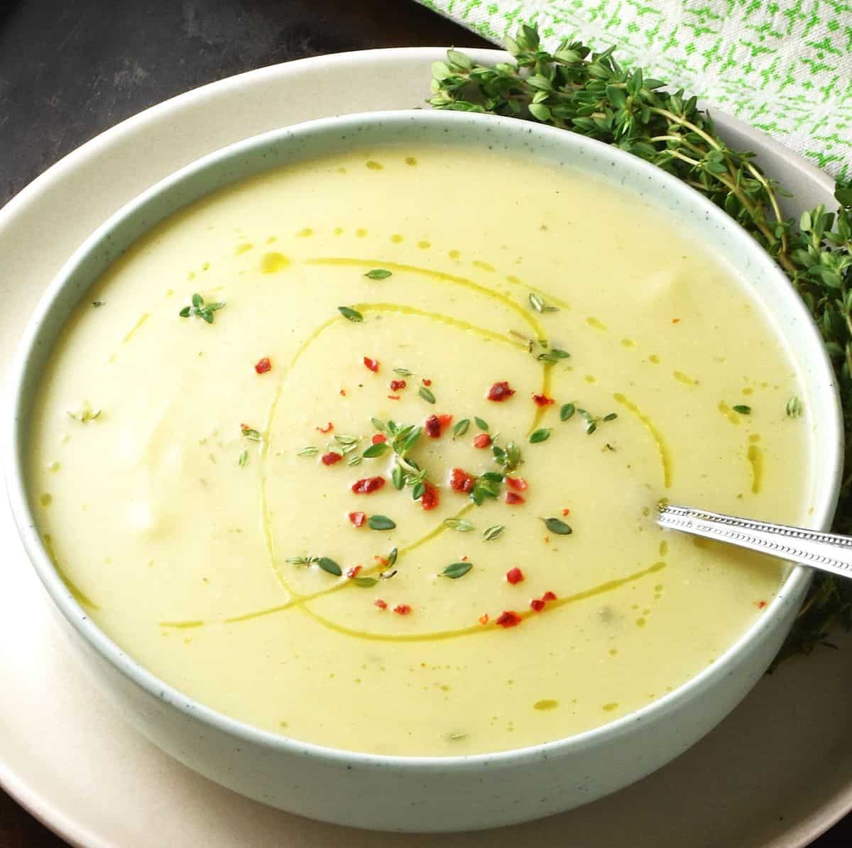 Side view of creamy cauliflower leek and potato soup in green bowl with fresh thyme in background.