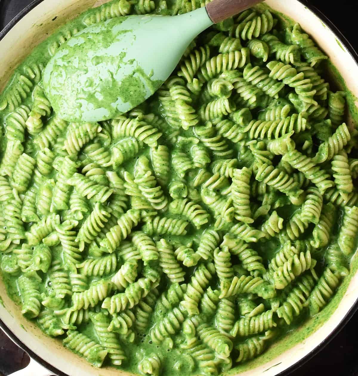 Fusilli pasta with creamy spinach sauce in large white pan with green spoon.