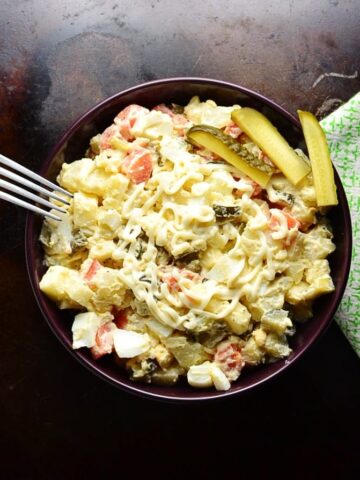 Top down view of Polish potato salad in purple bowl, with fork on the left and green cloth on the right on dark brown surface.