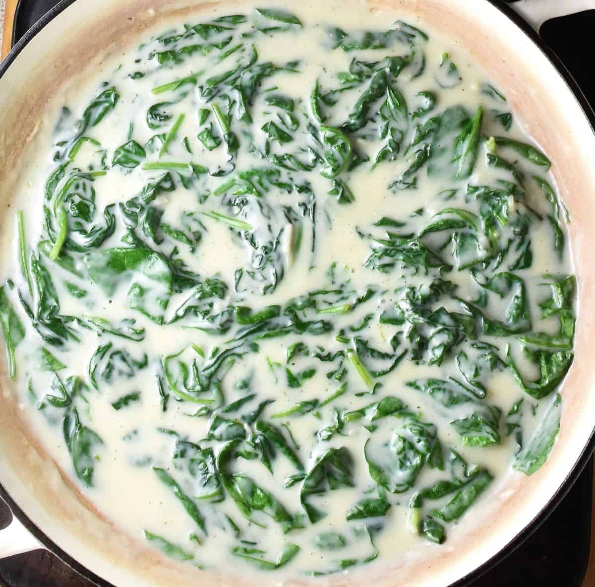 Creamy sauce with spinach in white pan.