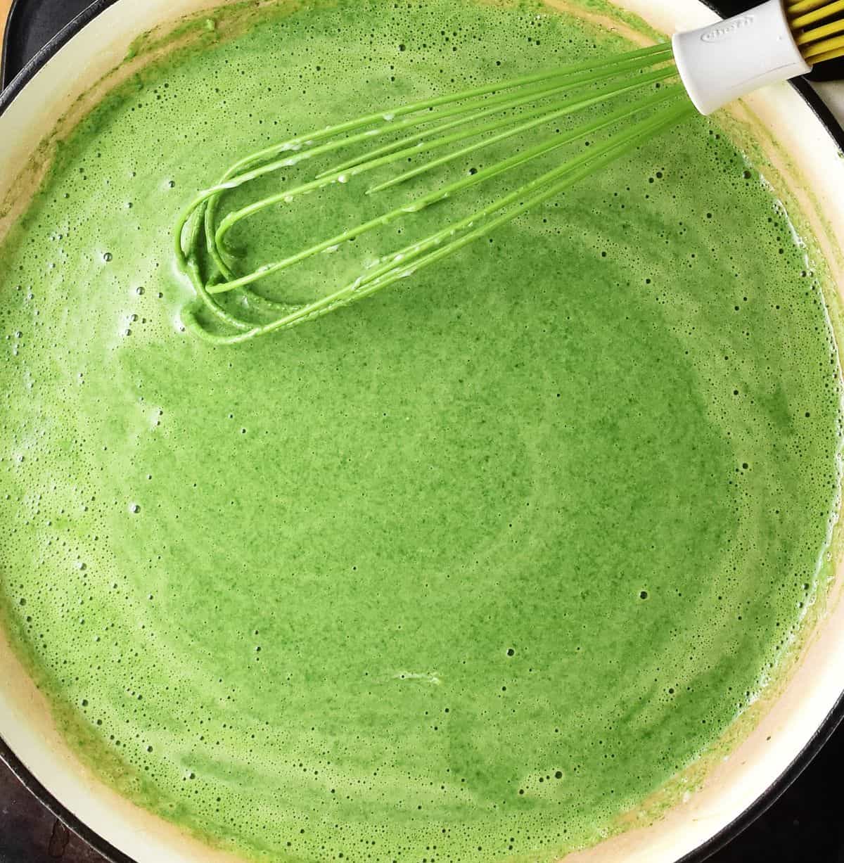 Vivid green spinach sauce with green whisk in parge shallow pan.
