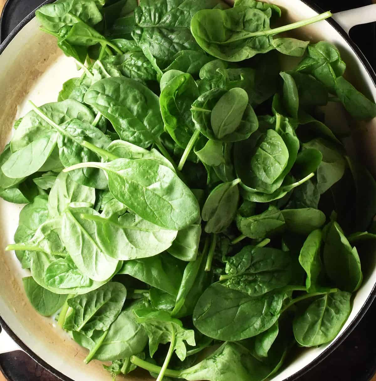 Fresh baby spinach leaves in white shallow pan with sauce.