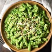Top down view of pasta with creamy spinach sauce in brown shallow bowl.