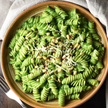 Top down view of pasta with creamy spinach sauce in brown shallow bowl.