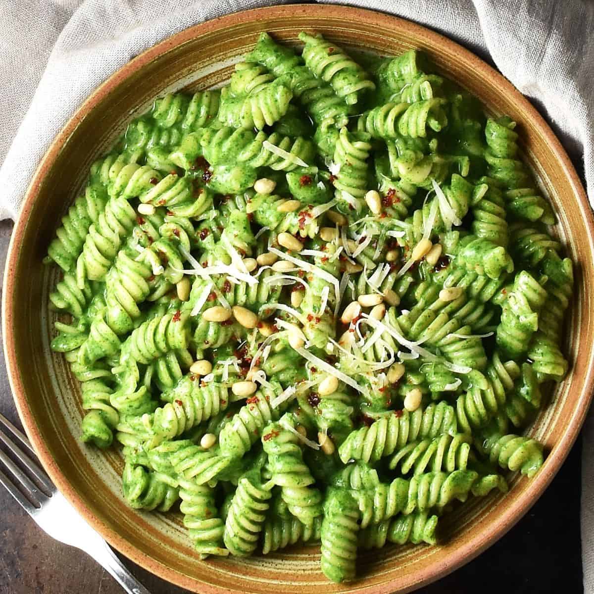 Top down view of pasta with creamy spinach sauce in brown shallow bowl.