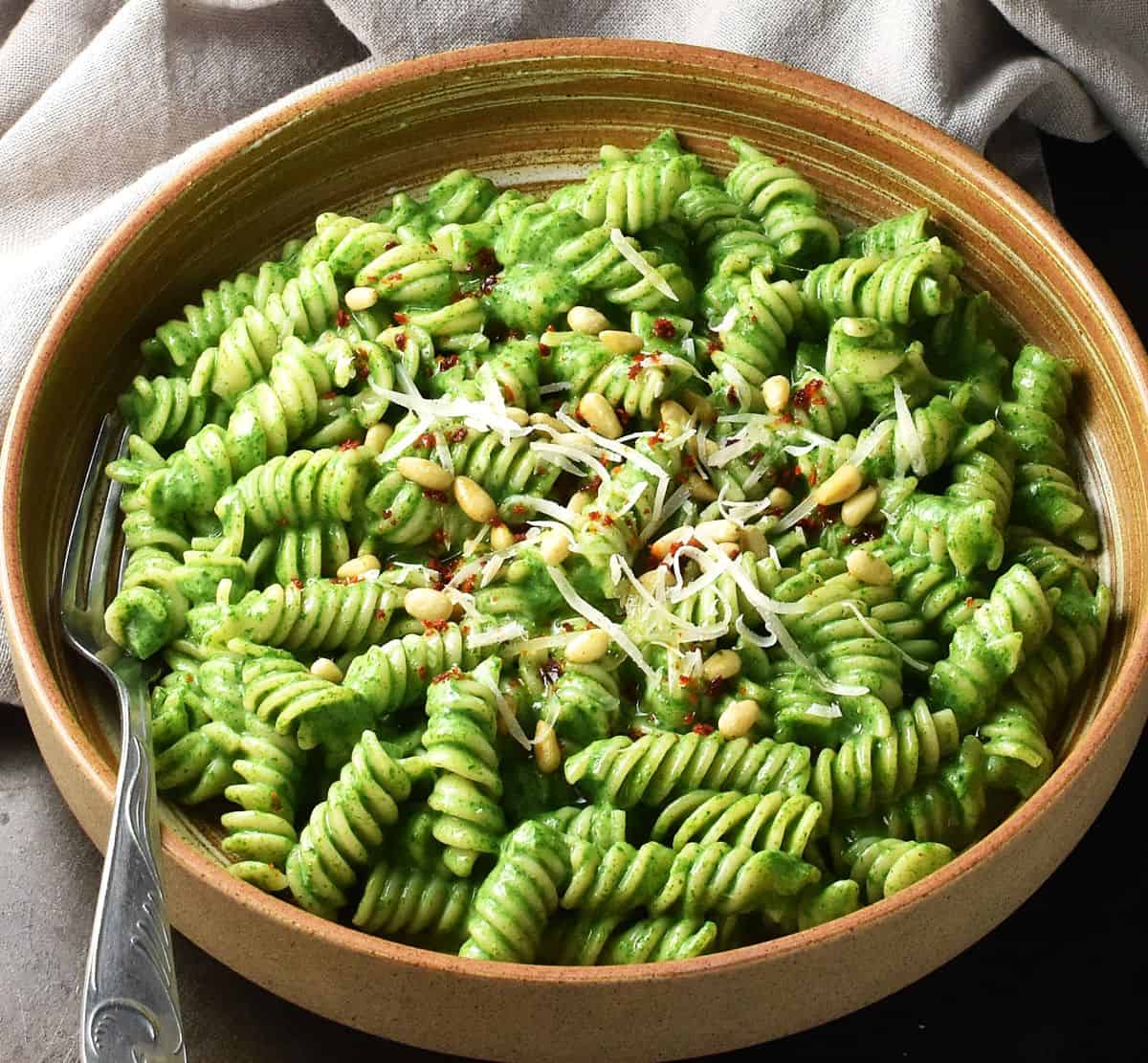 Side view of pasta with creamy spinach sauce in brown bowl with fork.