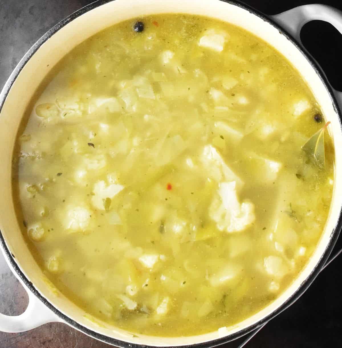 Soup with chunks of cauliflower, potato and leek in soup in large white pot.