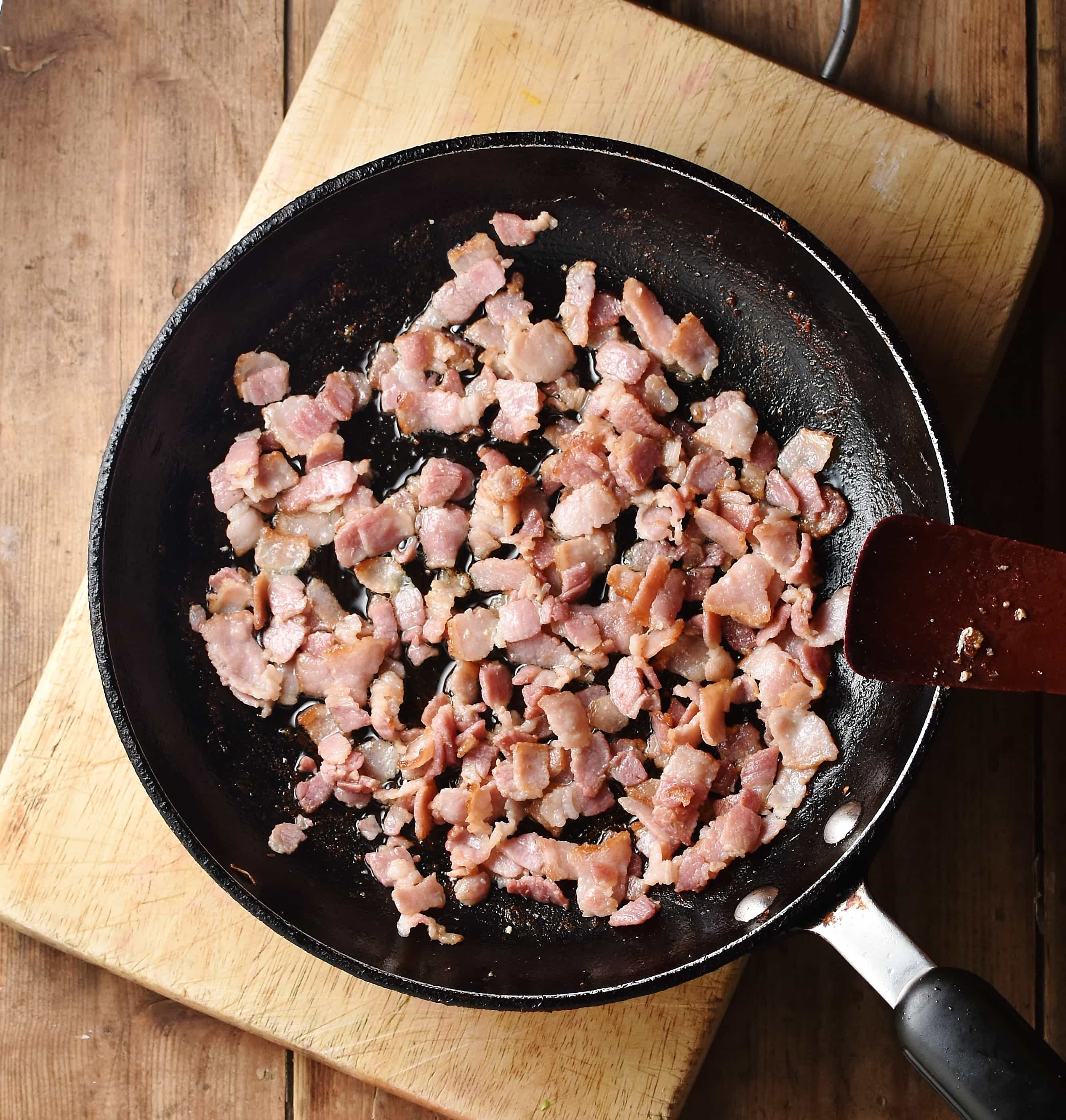 Bacon pieces in skillet on top of wooden board.