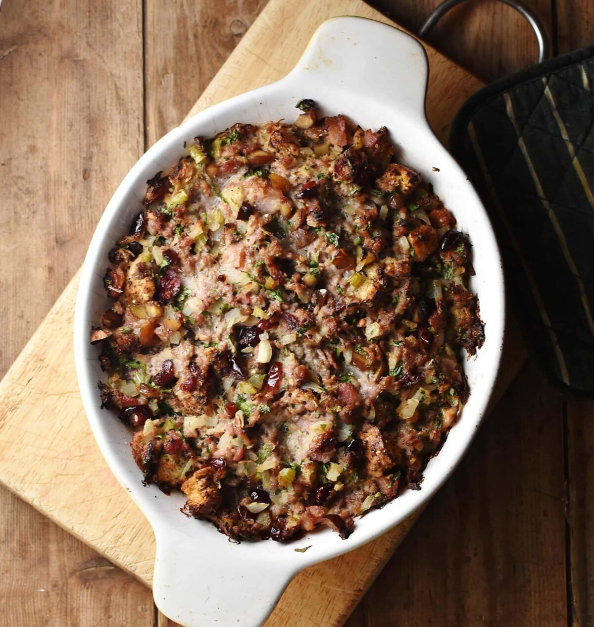Baked stuffing casserole in white oval dish on top of wooden board.