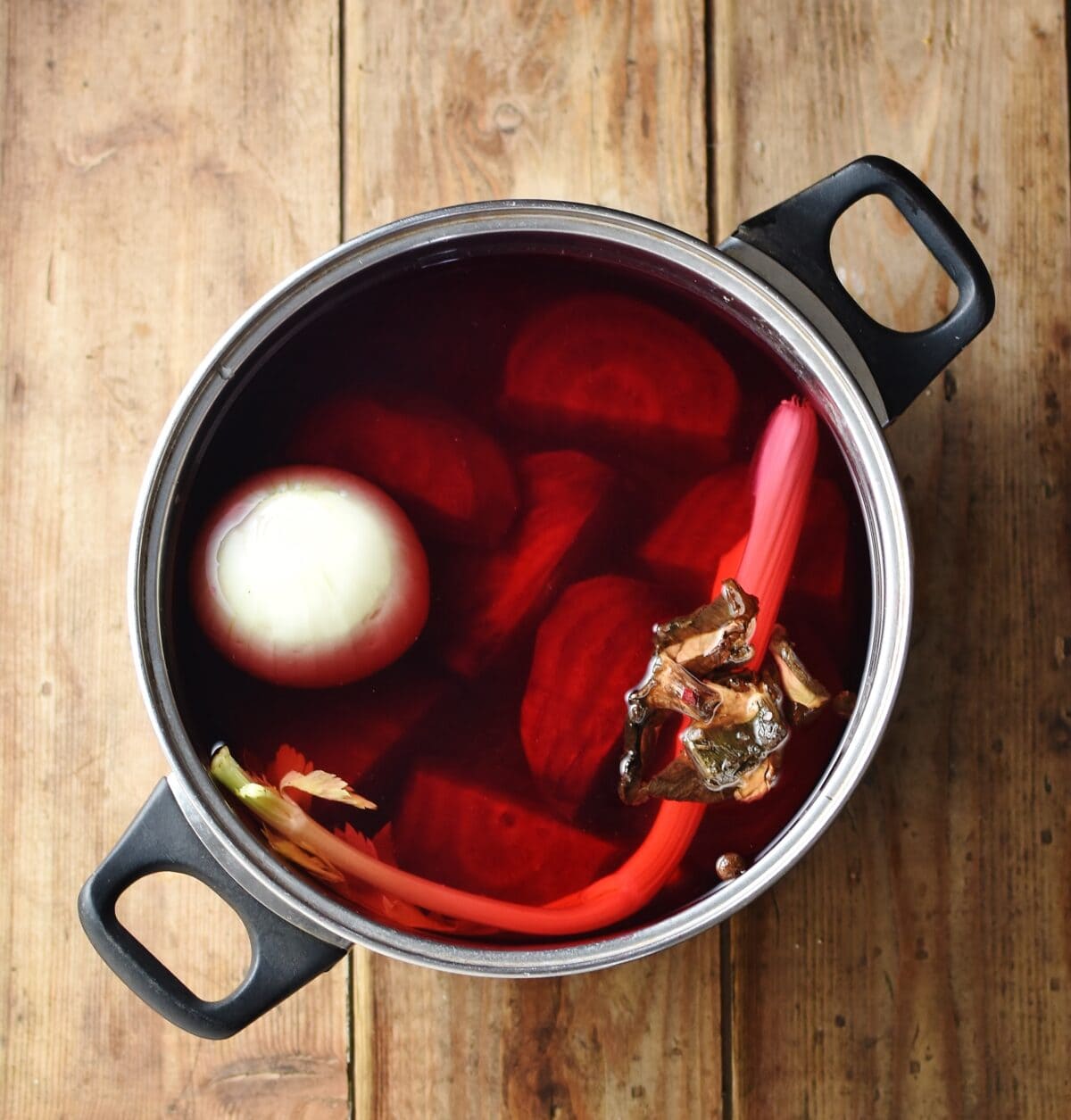 Onion, pieces of beetroot, wild mushrooms and celery stalk in large pot with water.
