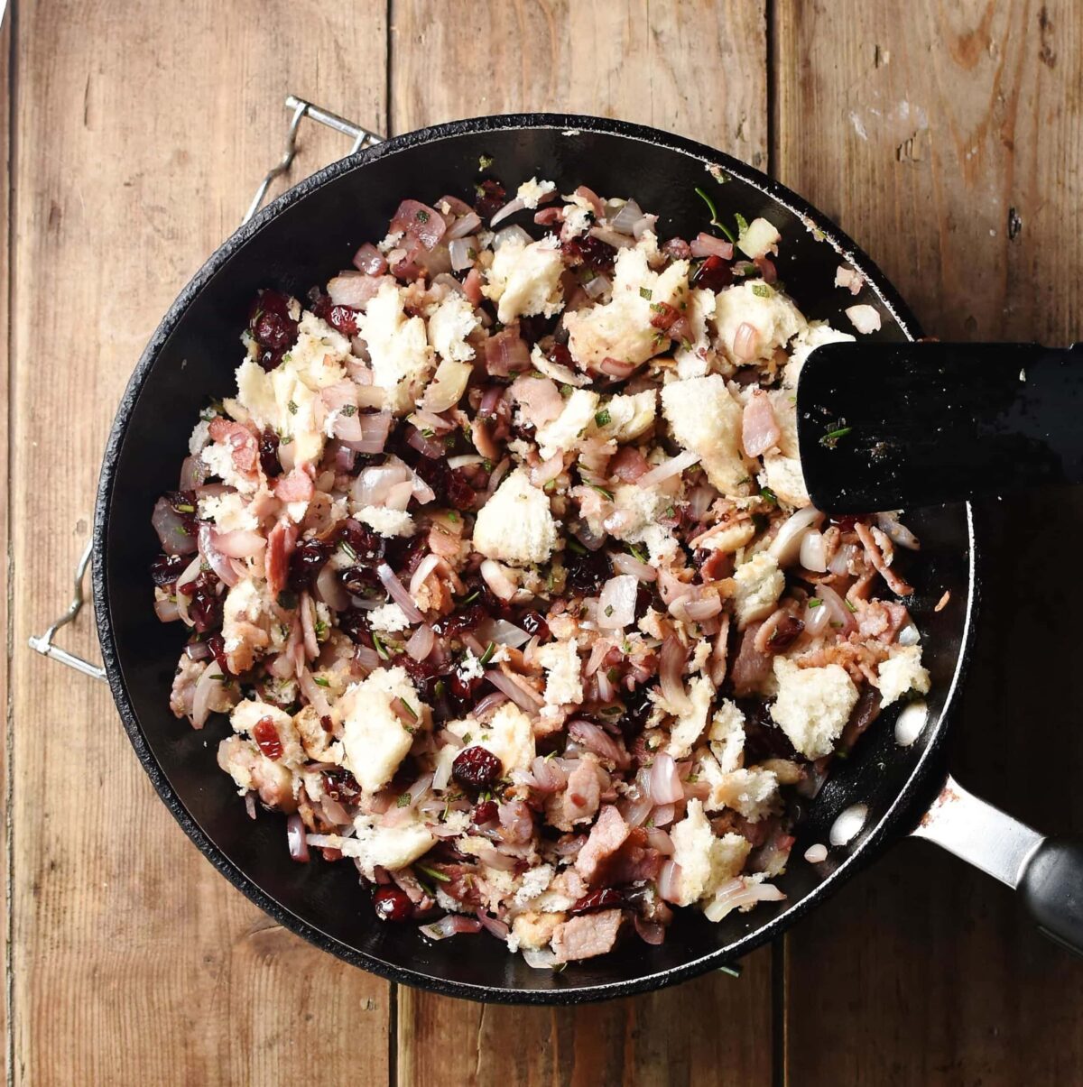 Onion, cranberry and bread mixture in skillet with black spatula.