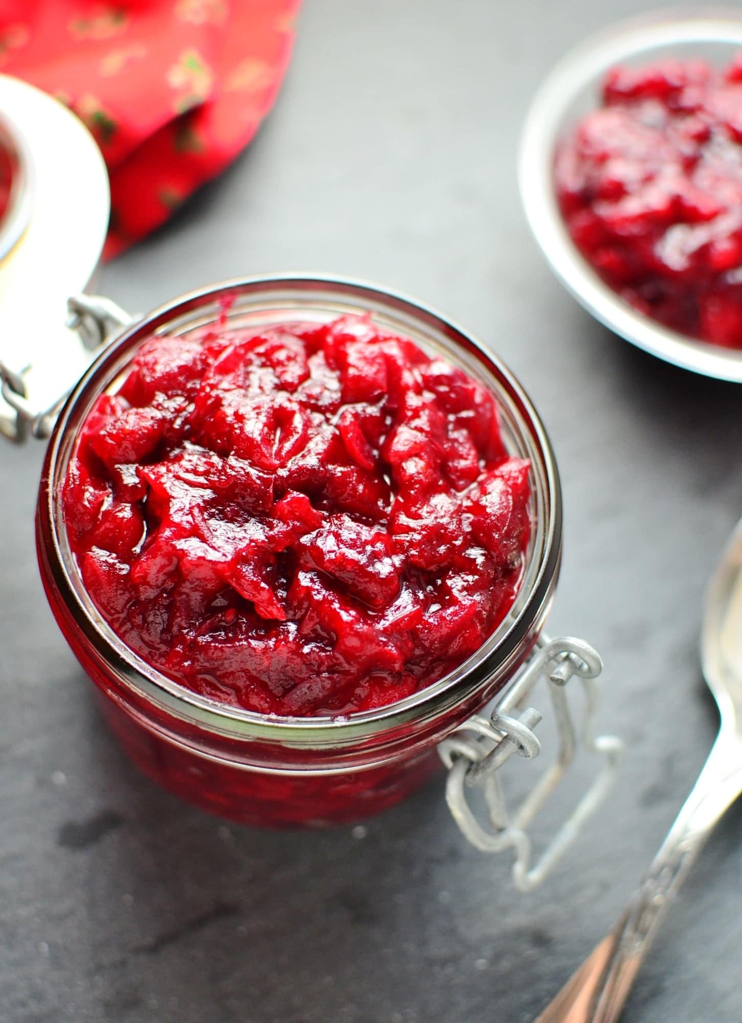 Top down view of cranberry sauce inside open jar with spoon in bottom right corner on top of grey surface.