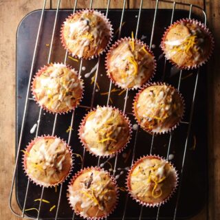 Muffins with icing and orange zest on top of rack.