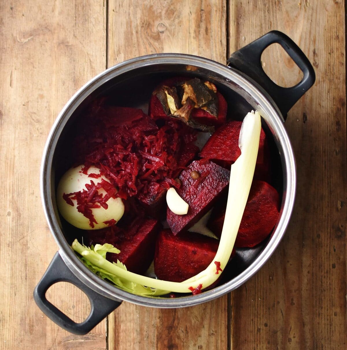 Pieces of beetroot, onion, grated beet, celery, garlic clove and wild mushrooms in large pot.