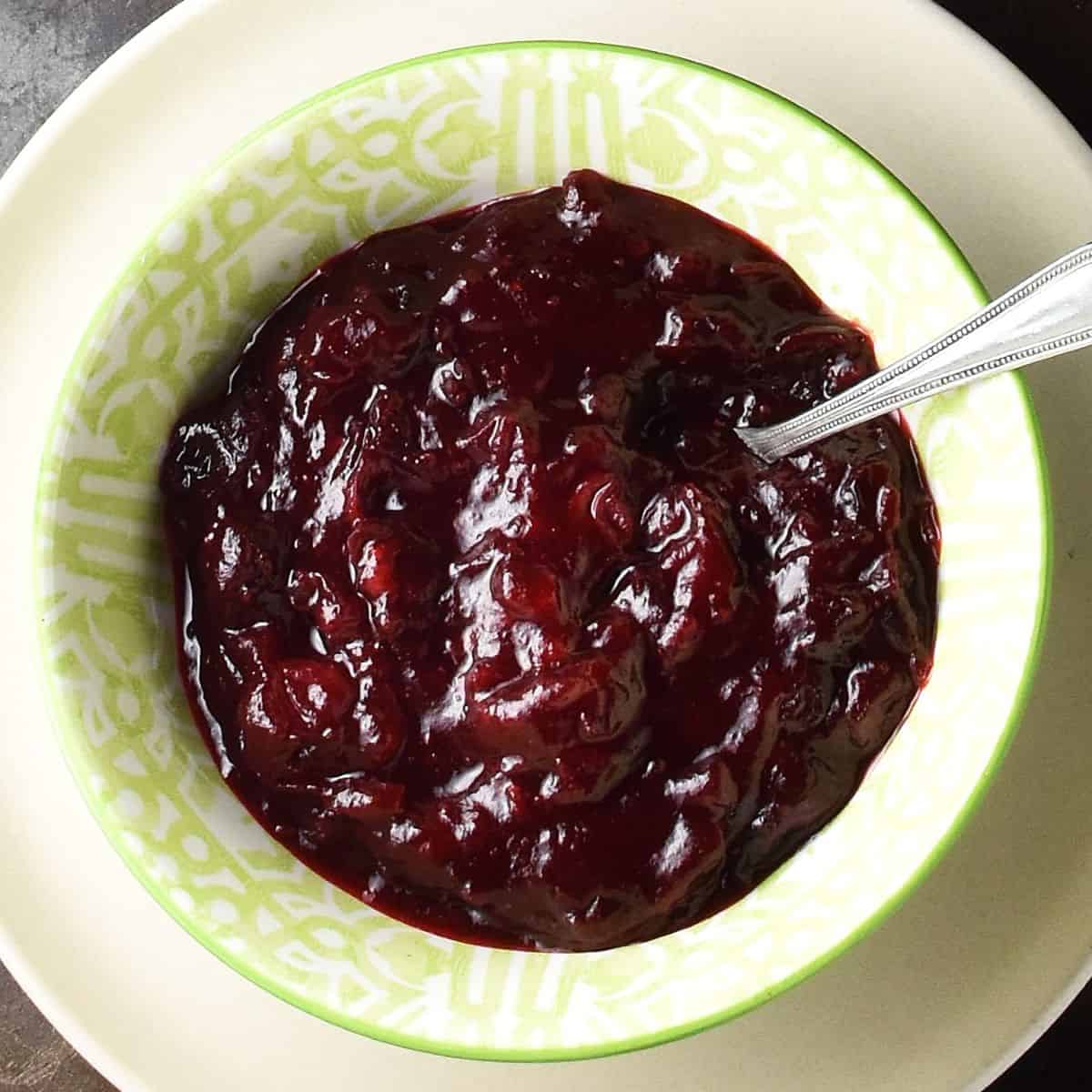 Top down view of cranberry sauce with honey in green bowl with spoon.