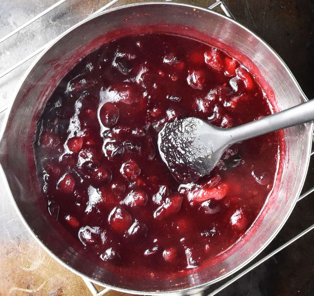 Top down view of thick cranberry sauce with honey in saucepan with black spatula.