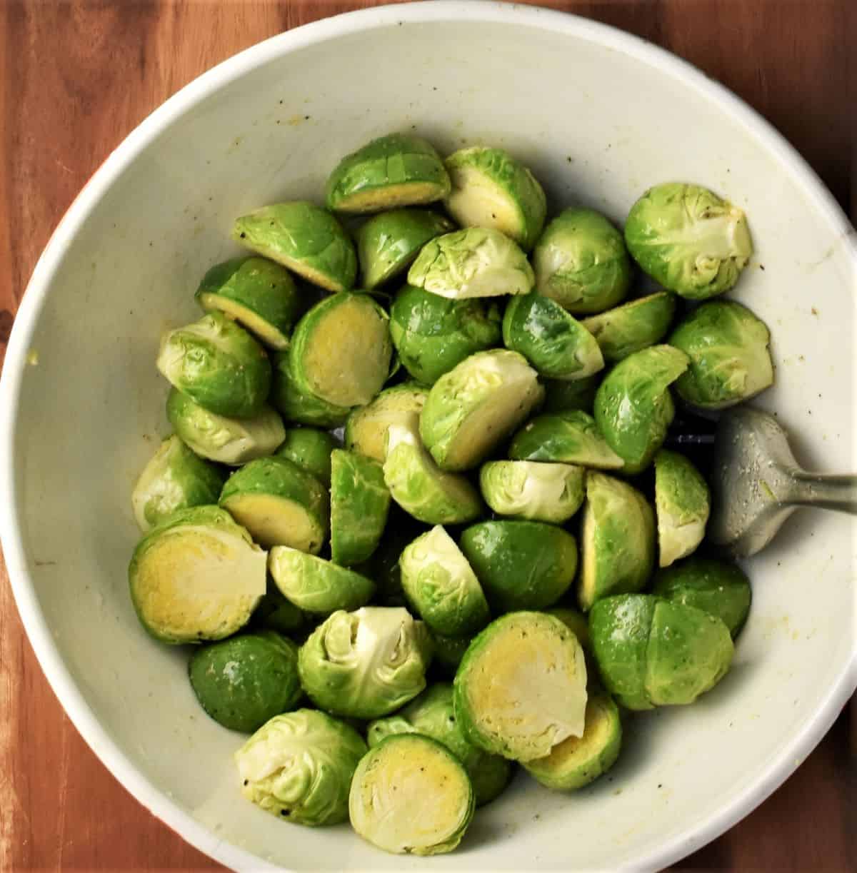 Halved brussels sprouts coated in oil in white bowl.