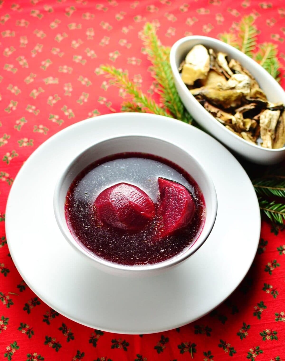 Beetroot soup with beetroot pieces in white bowl on top of white plate with spoon to the right.