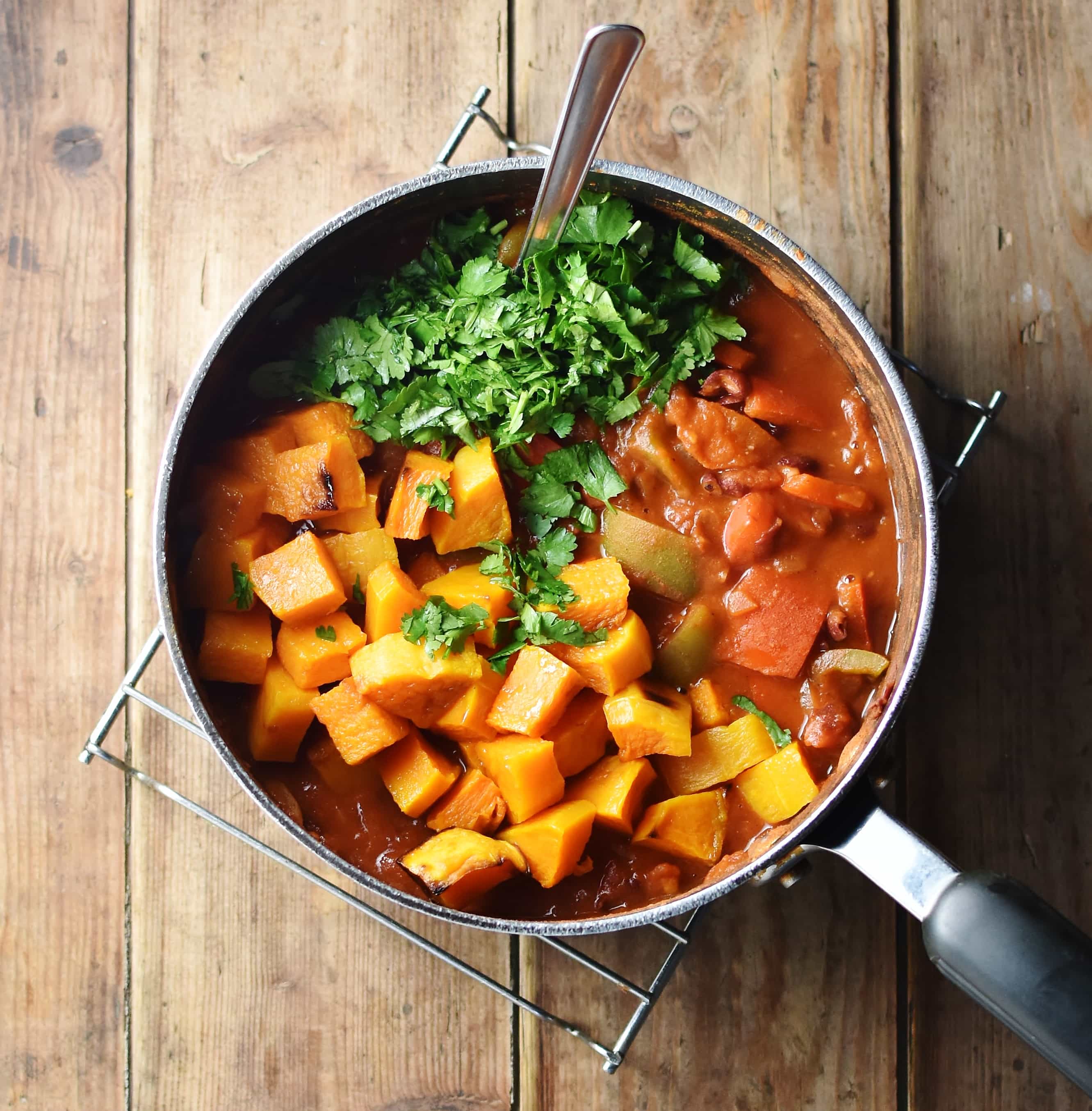 Cubed squash, herbs and tomato sauce in large pot with spoon.