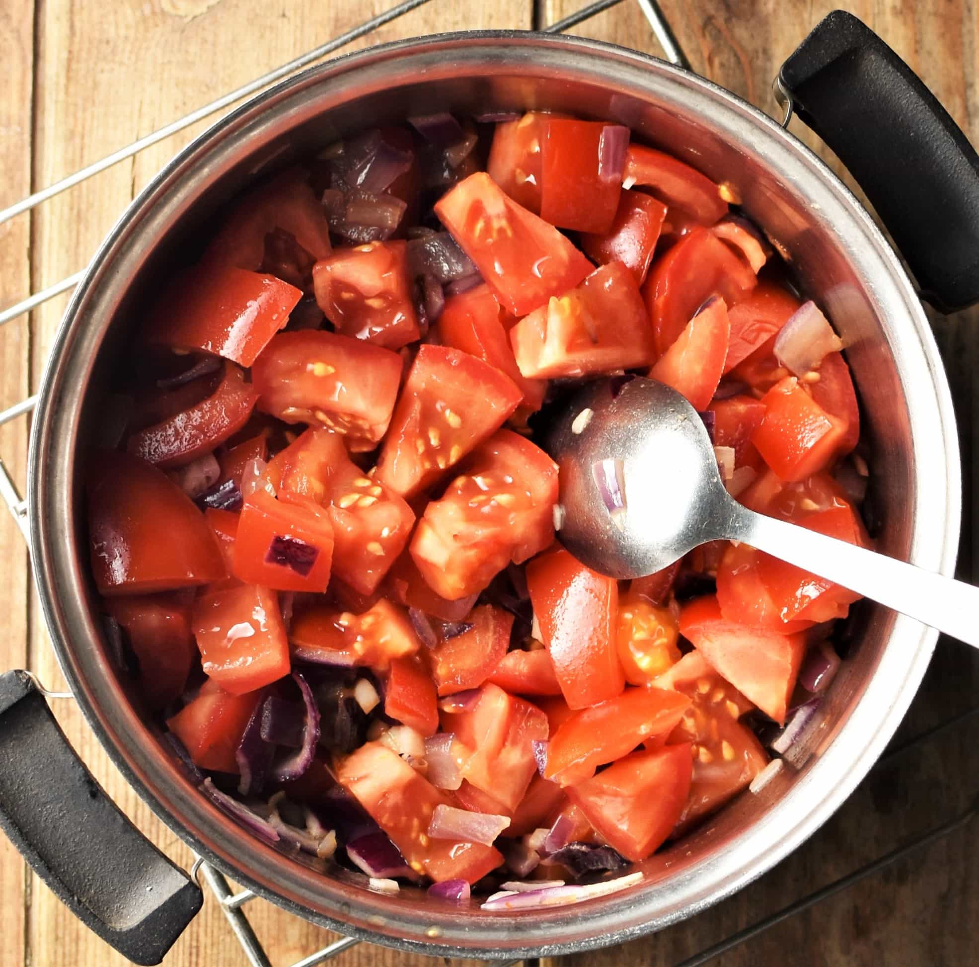 Chopped tomatoes in pot with spoon.