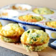 Asparagus egg muffins on wooden board with ceramic muffin tin in background.