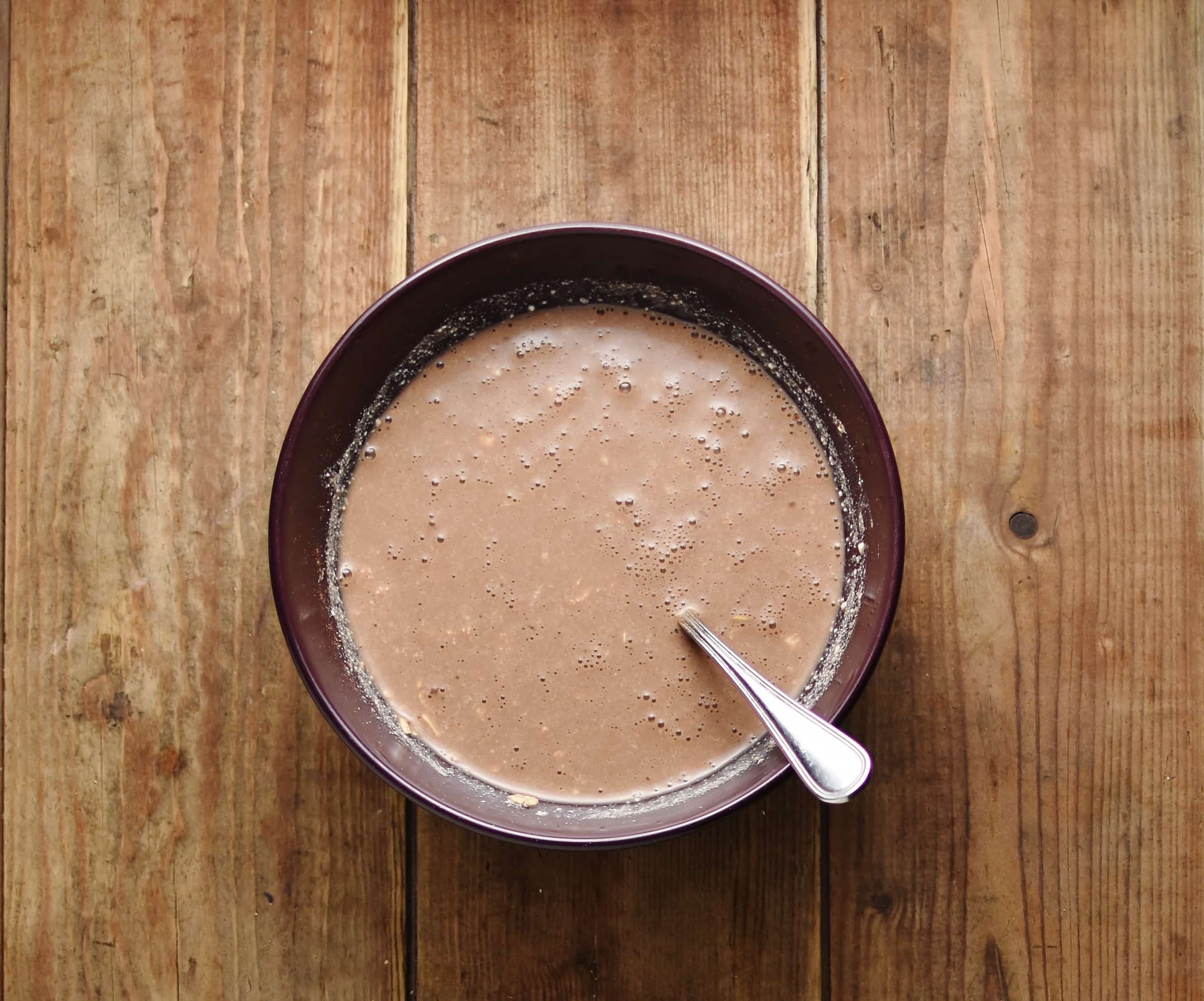 Chocolate overnight oats mixture with spoon inside purple bowl.