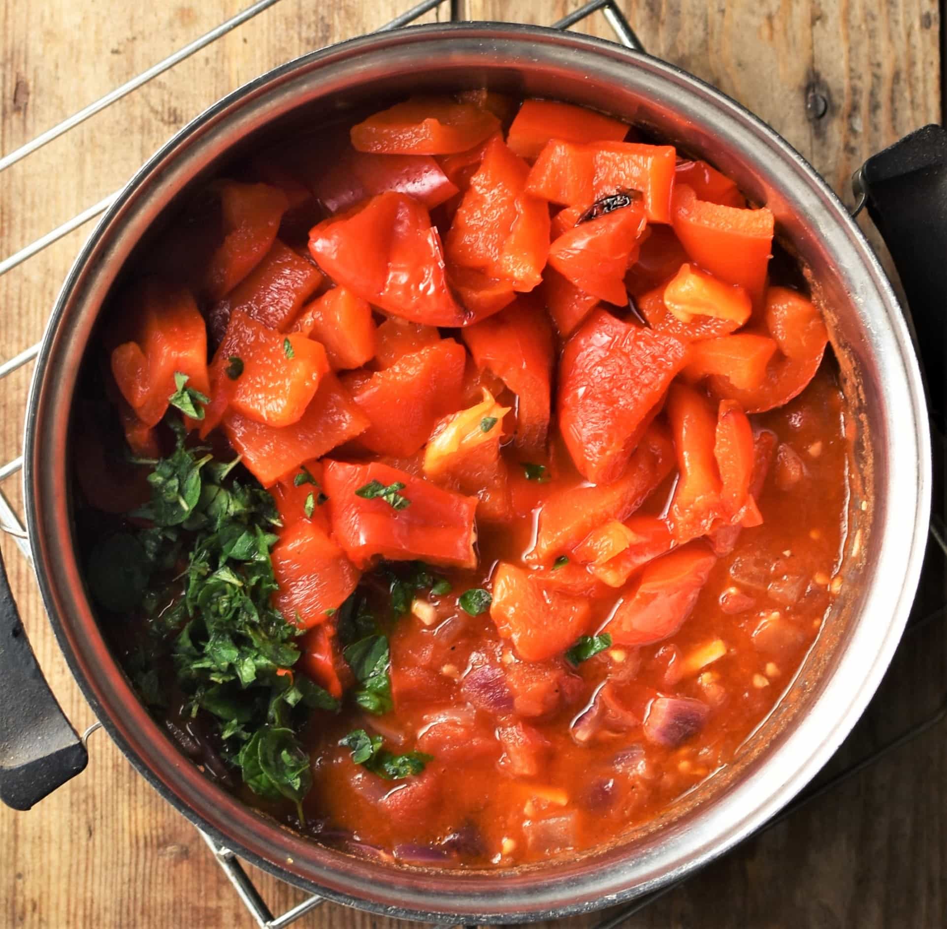 Chopped red peppers, tomato sauce and herbs in pot.