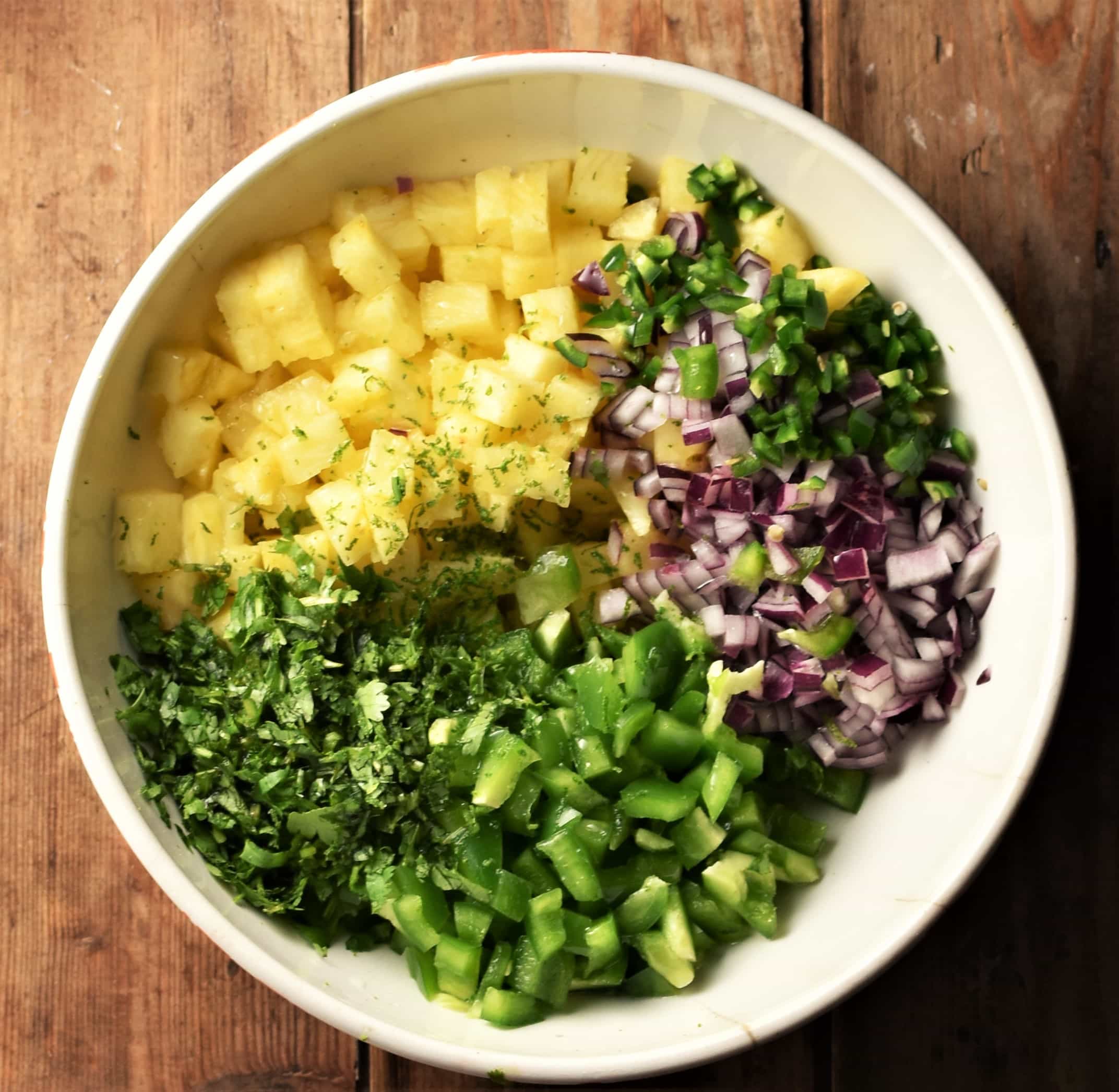 Chopped pineapple, green pepper, cilantro and red onion in white bowl.