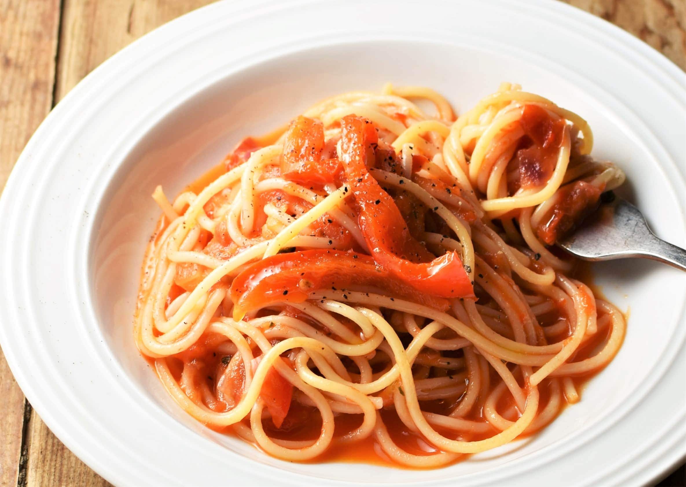 Side view of red pepper pasta with tomato sauce on white plate with fork.
