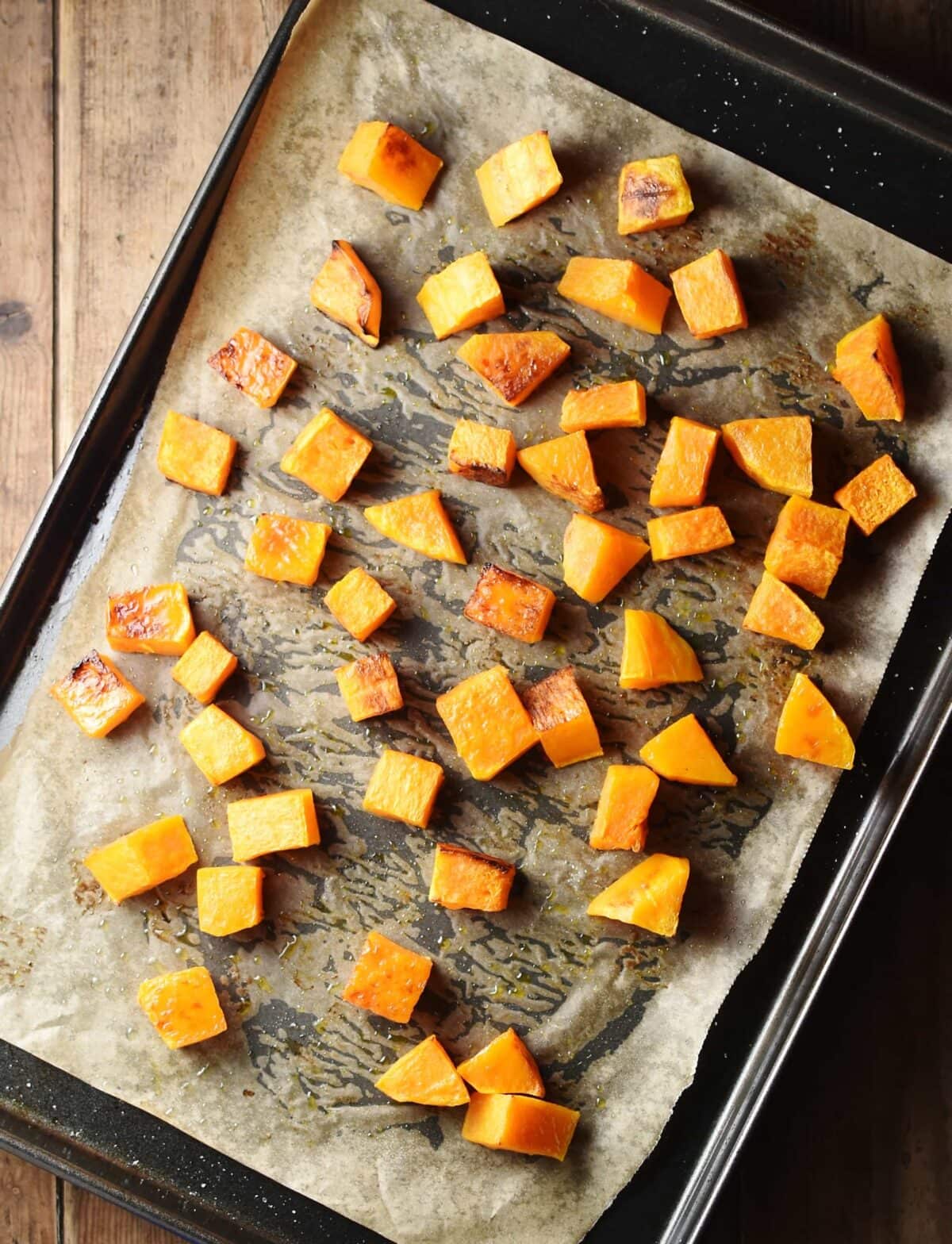 Butternut squash cubes on top of oven tray lined with parchment paper.