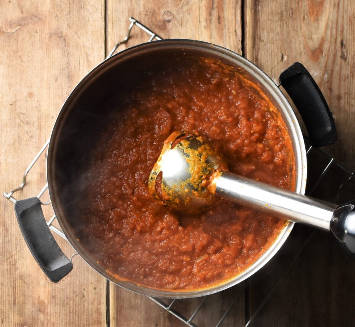 Pureed tomato sauce in pot with hand blender end piece.