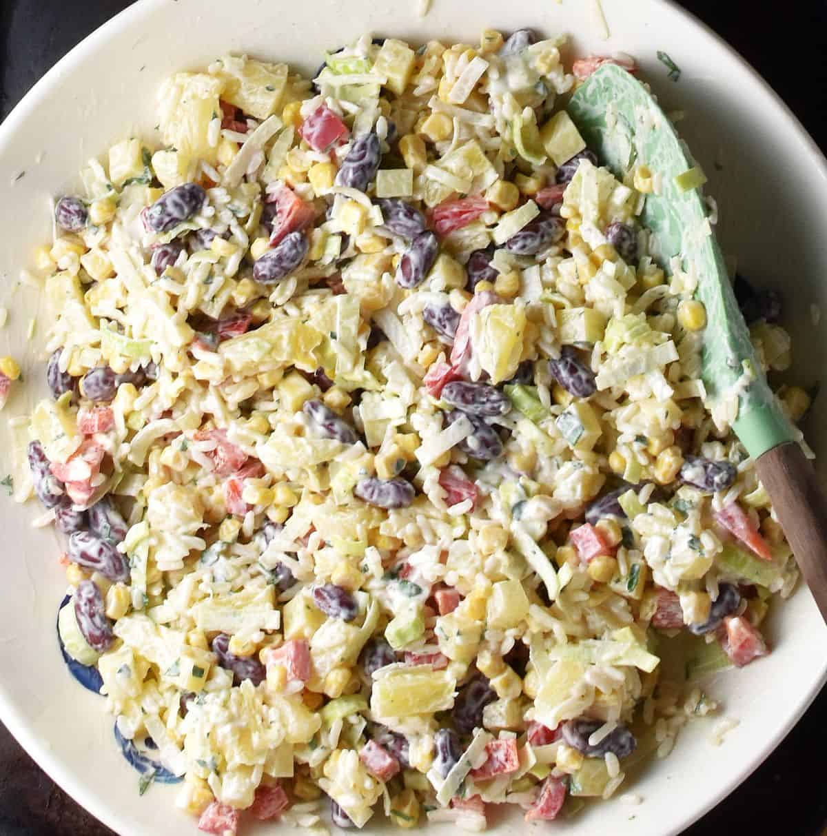 Top down view of pineapple corn salad ingredients mixed together in white shallow bowl with green spoon.