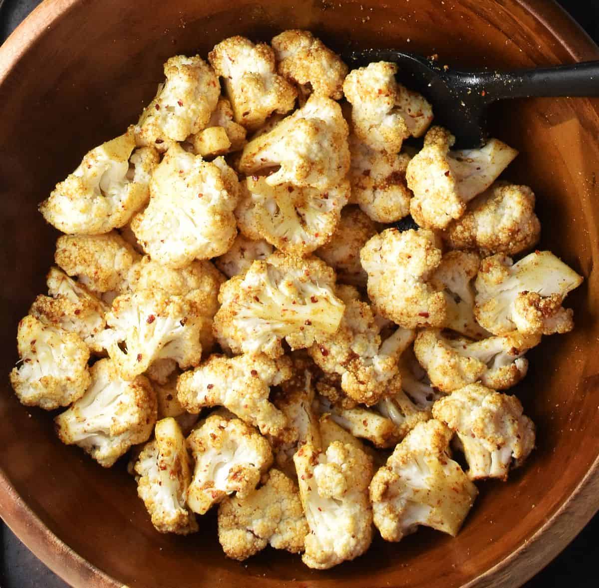 Cauliflower florets coated in curry spice mixture in large wooden bowl.
